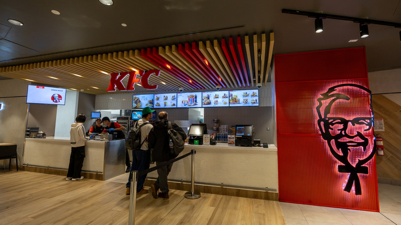 Customers wait in line at a KFC with the logo on the wall