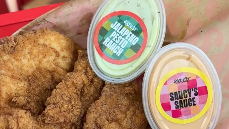 Two containers of KFC's Saucy brand sauces with chicken tenders in a basket