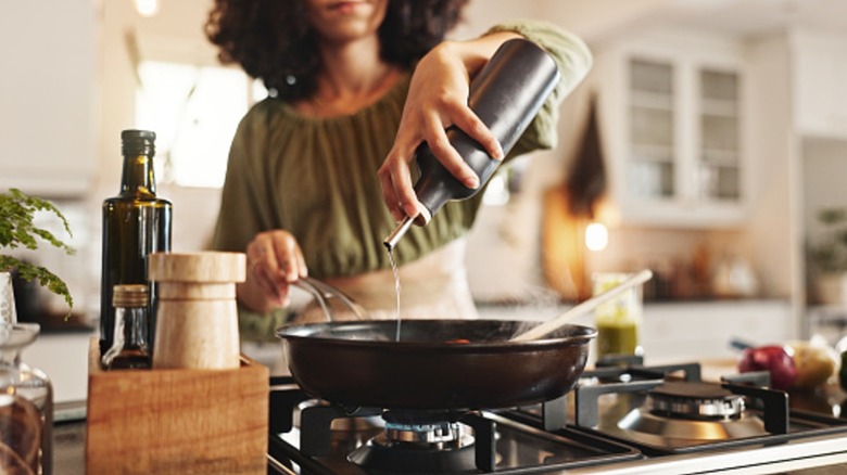 A woman cooking in a kitchen, pouring oil into a pan.