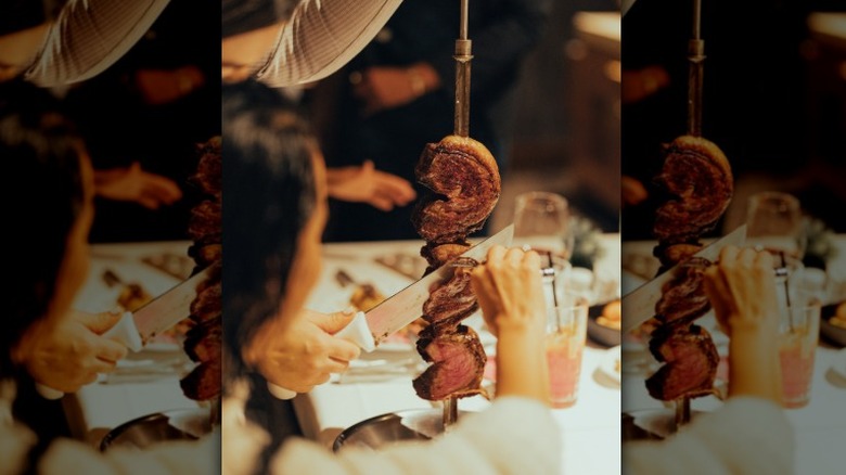 A gaucho chef slicing meat off the skewer