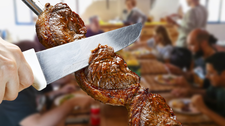 A knife slicing meat off of a skewer