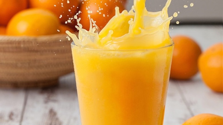 glass of orange juice splashing and bowl of oranges
