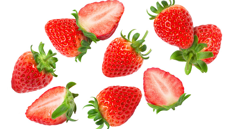 Sliced and whole strawberries falling against a white background