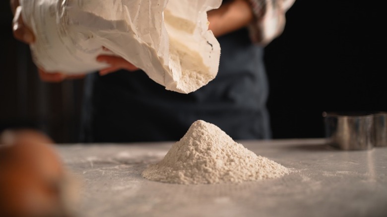 A baker pours flour from a bag onto a kitchen countertop