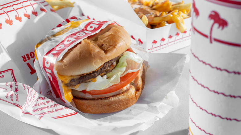 A cheeseburger from In-N-Out half-wrapped in paper beside fries and a drink