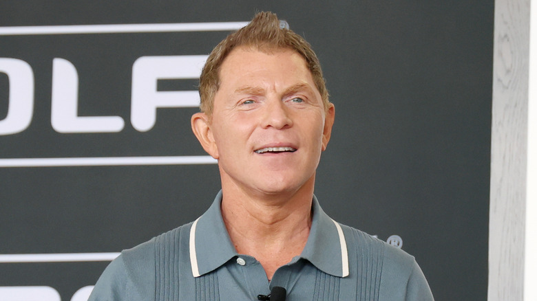 Bobby Flay smiling during an event wearing a blue polo