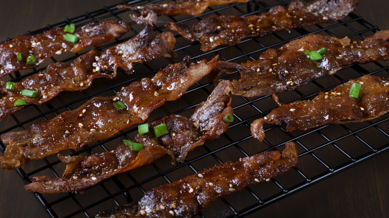 Pieces of maple-glazed bacon on a cooling rack with green onions sprinkled on them