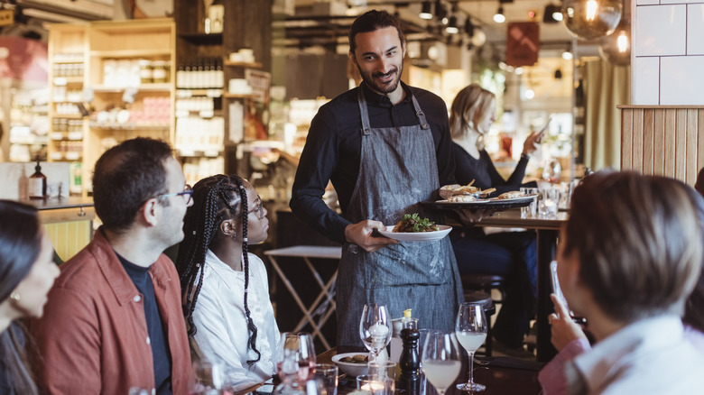 A waiter serving a table of customers their food at a restaurant.