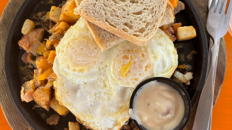 Over-easy egg on top of hash brown potatoes with bread on a plate.