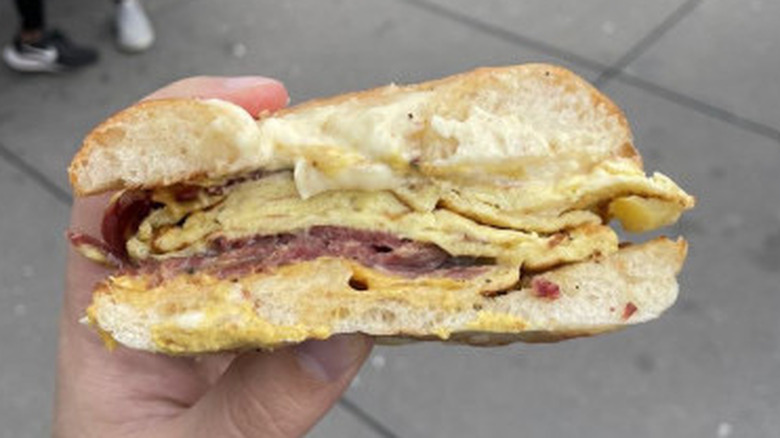 Hand holding a pastrami, egg, and cheese