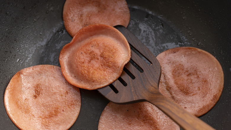 Slices of fried bologna being flipped with a spatula in a skillet.