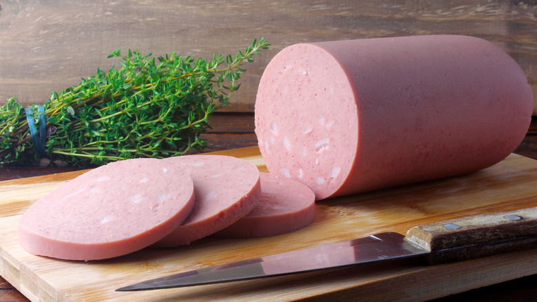 Whole and sliced bologna on wooden cutting board