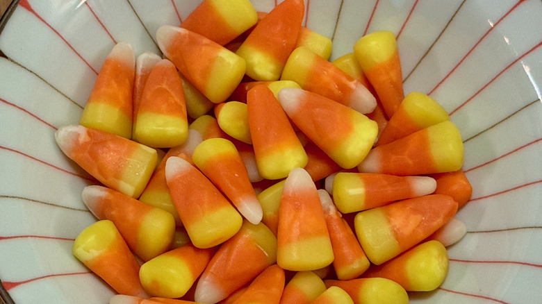 Orange, yellow, and white pieces of candy corn in a small striped bowl