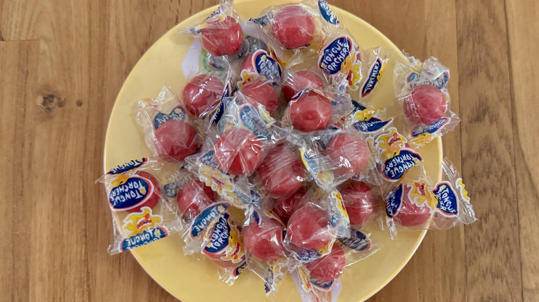 Plastic wrapped red jawbreakers on a small yellow plate.
