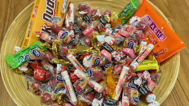 A bamboo bowl filled with an assortment of candies including Smarties, Laffy Taffy, peppermints, butterscotch, and Milk Duds