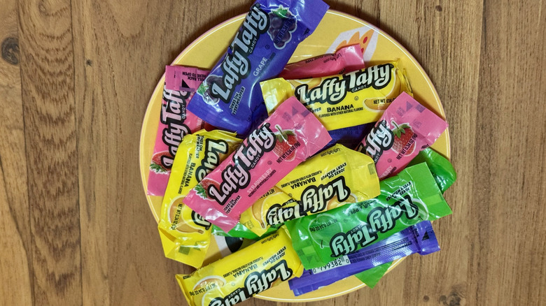 A small yellow plate stacked with pink, yellow, green, and blue packages of Laffy Taffy