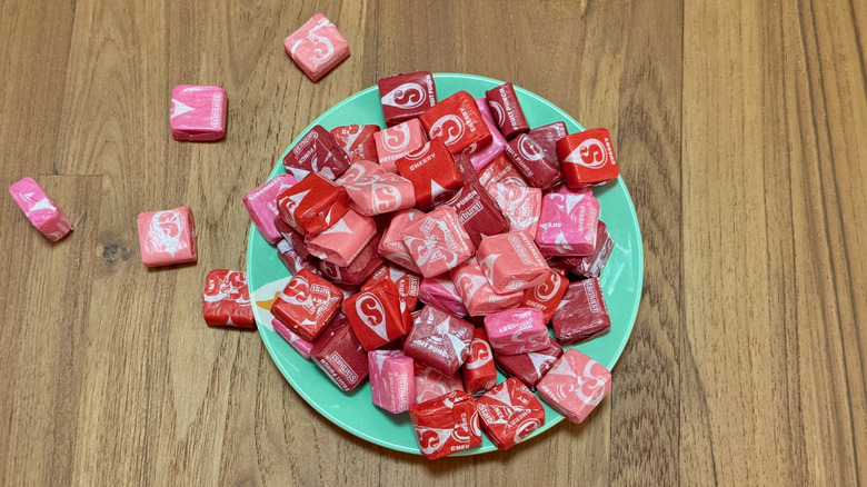 A pile of Starburst on a small turquoise plate with a few spilling onto the wooden table beside it