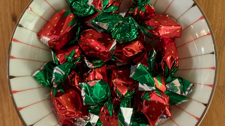 A small bowl filled with strawberry bon bons in red and green wrappers.