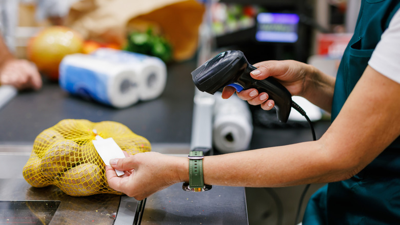A cashier at a grocery store scans a bag of potatoes.