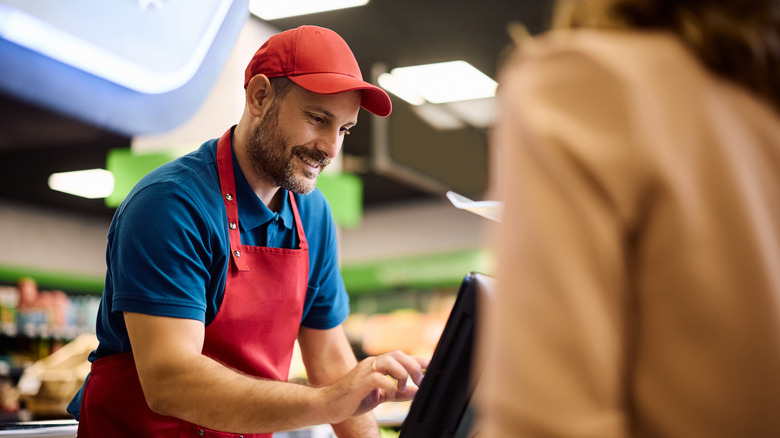 A male grocery store clerk cashes a customer out.