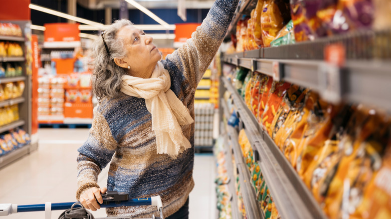 A senior woman grocery shopping and reaching on a top shelf for something