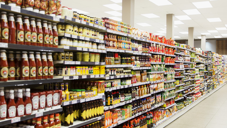A picture of a row of grocery shelves, stocked with condiments and other products.