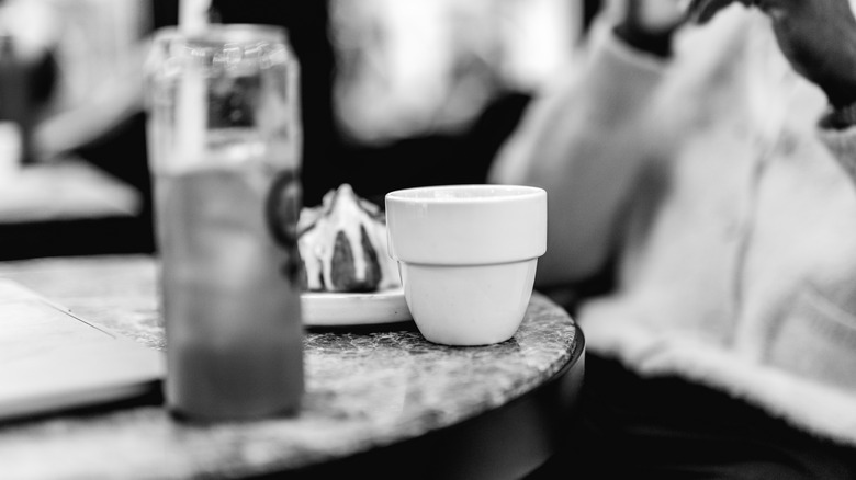 A black and white photo of a cup of coffee on a table with a pastry