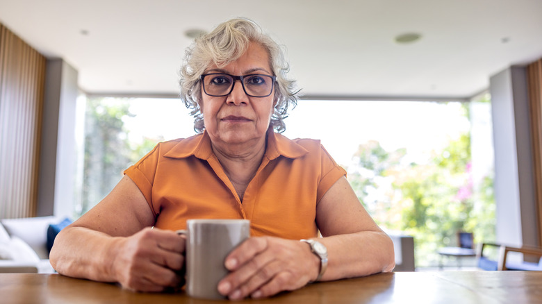 A woman looking at the camera while drinking coffee at home