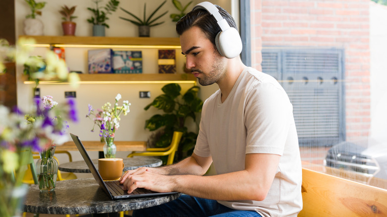 Man on a laptop in a cafe, wearing headphones