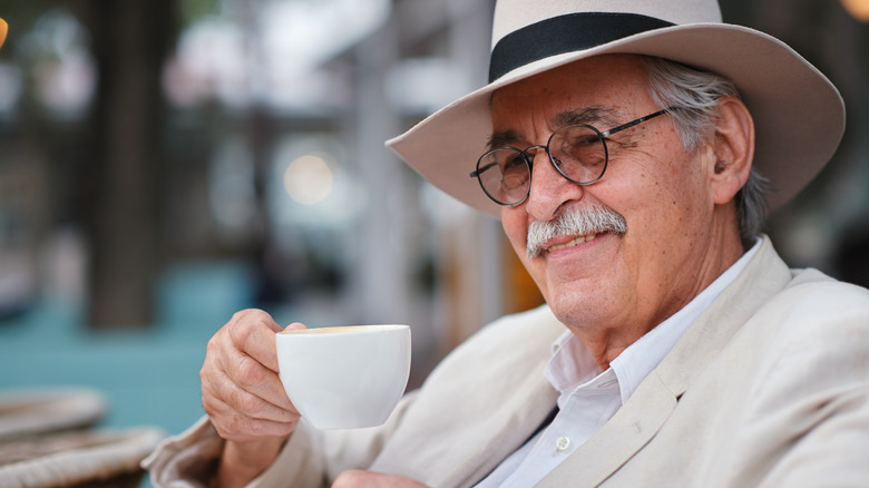 An older man in a hat enjoying a coffee