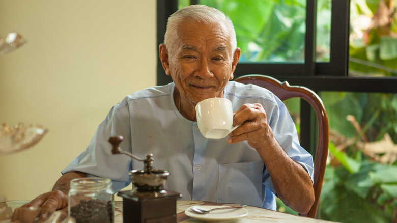 Older man drinking coffee at a table and smiling at camera