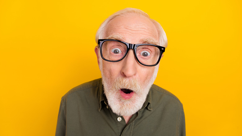 Older man with a shocked look on his face, against a yellow background