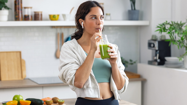 Shot of kind sporty woman drinking a healthy green smoothie standing in the kitchen at home.