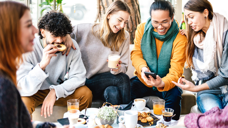 Multicultural friends playing with mobile phone at coffee bar
