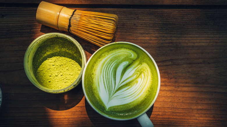 A cup of matcha latte on wooden table under sunlight.