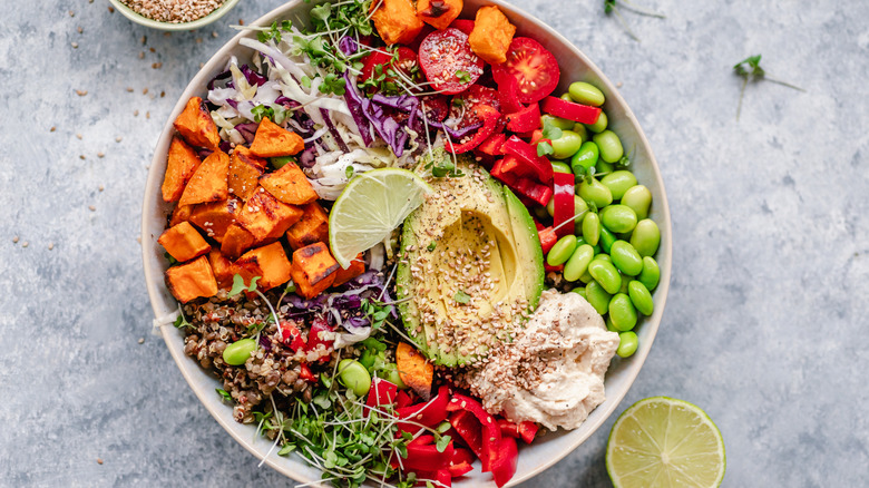 Overhead view of a colourful vegan bowl with quinoa, sweet potato, avocado, hummus and variety of veggies