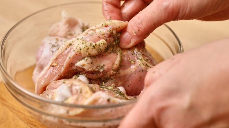 Hand marinating chicken in a bowl.