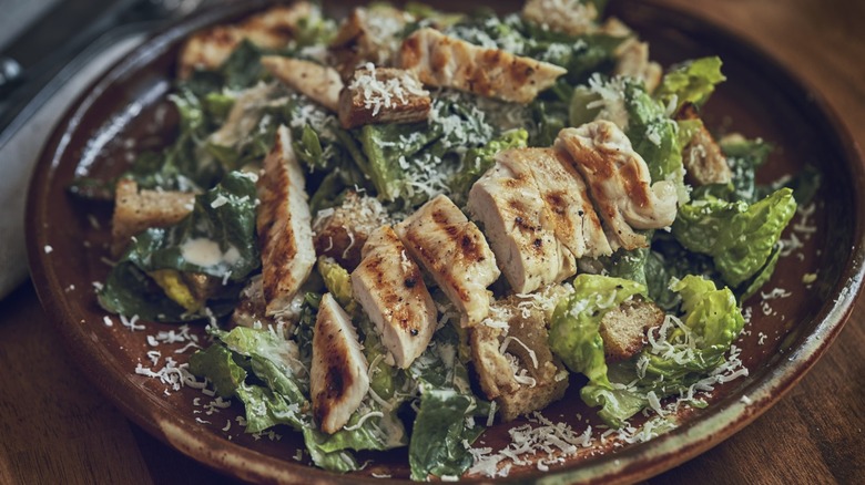Homemade chicken Caesar salad on brown plate.