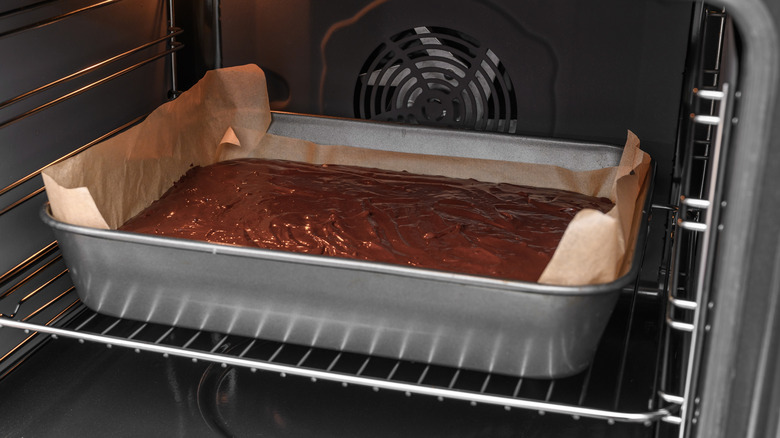 A partially cooked chocolate cake in a parchment-lined rectangular metal pan in the oven.