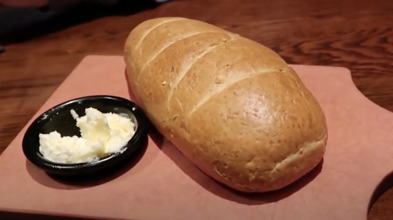 Loaf of Longhorn Steakhouse bread with whipped butter on the side, served on a wooden cutting board
