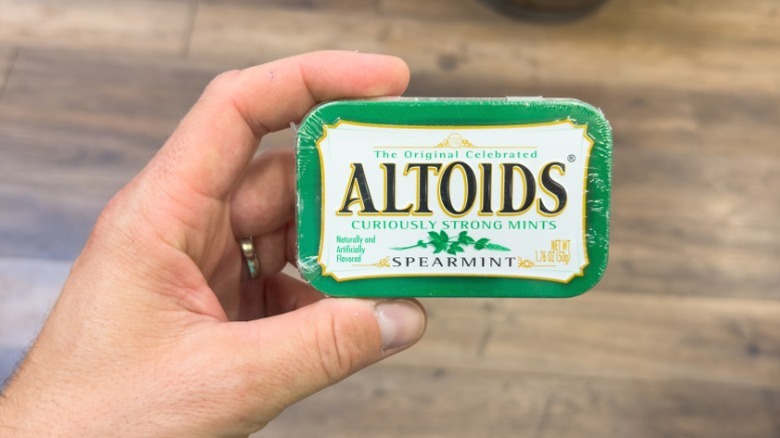 A hand holding a tin of Altoids.