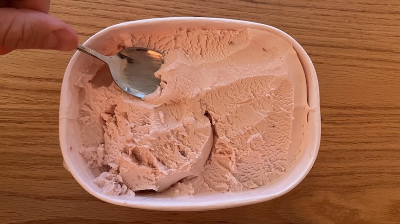 Spoon scooping strawberry ice cream from a carton
