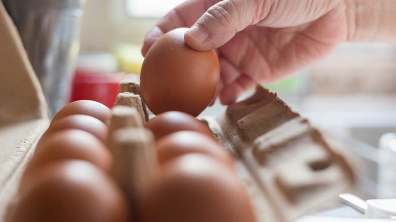 Hand picking up single egg out of a carton