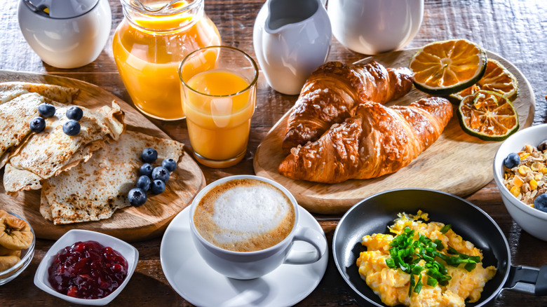 Crepes, croissants, scrambled eggs, coffee, and orange juice artfully arranged on table