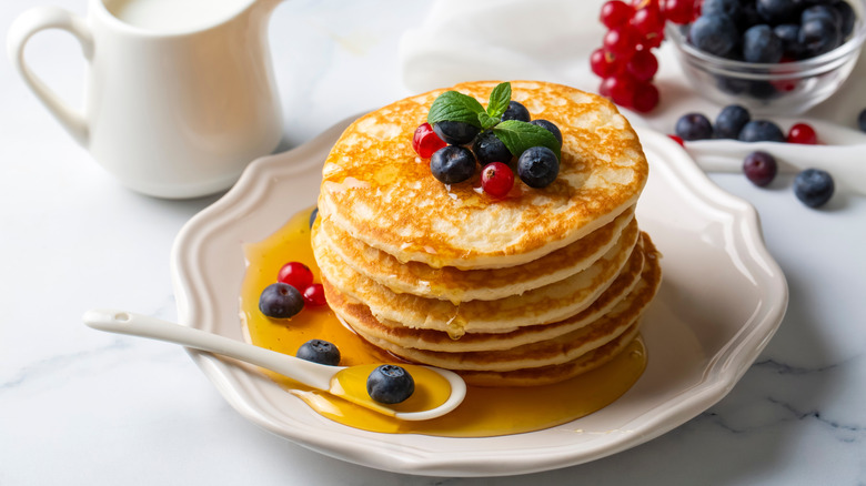 Stack of pancakes on white plate topped with berries