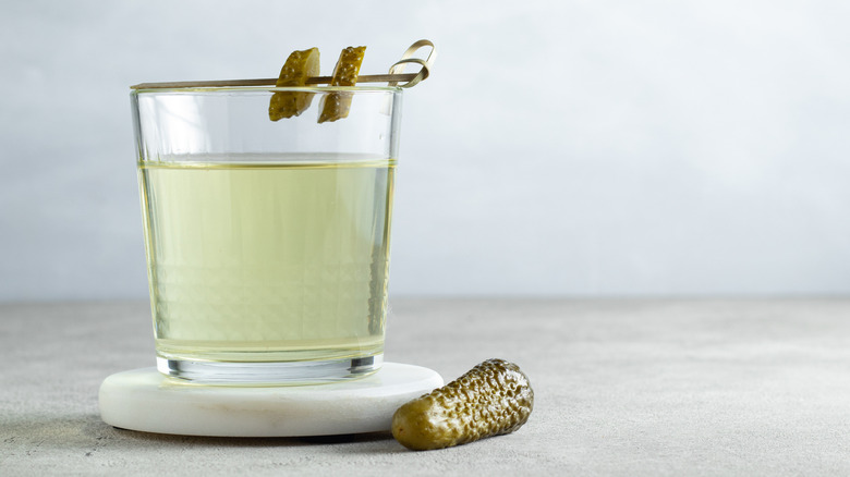 A cup of pickle juice garnished with pickle slices