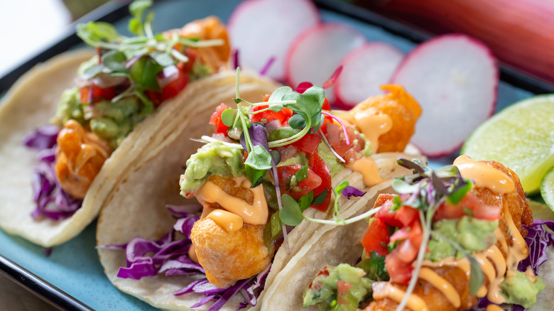 Three seafood tacos with guacamole, cabbage, and pico de gallo