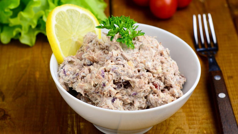 Moist tuna salad in a white bowl with a lemon as a garnish