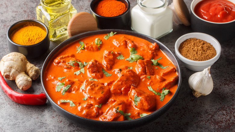 A bowl of chicken tikka masala surrounded by raw ingredients