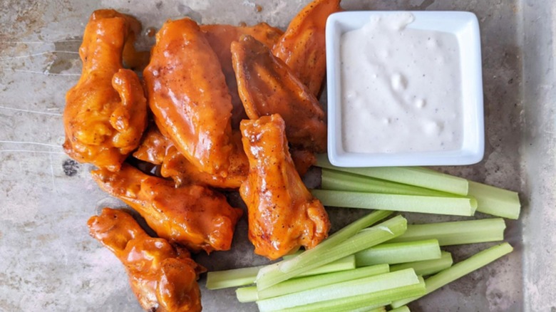 An overhead view of Buffalo chicken wings, sliced celery, and ranch dressing